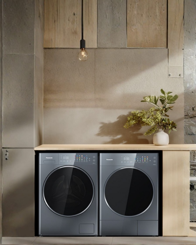 Bundle promo: Panasonic washer-dryer pair in a recessed laundry nook with warm concrete walls, a wooden countertop, and a potted plant.