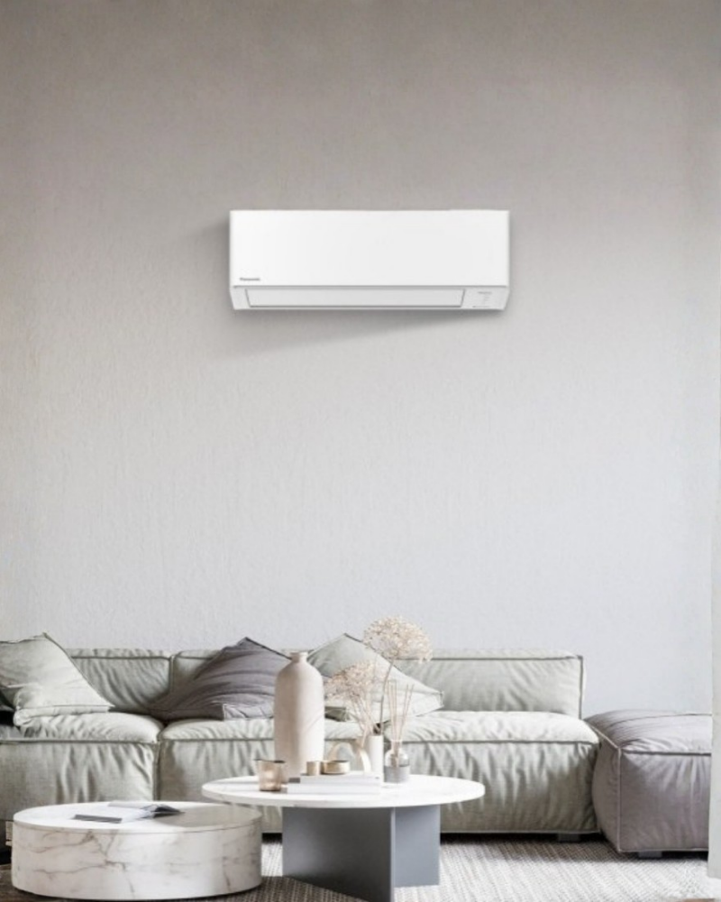 Panasonic X-Deluxe inverter air conditioner above a sofa in a minimalist living room.