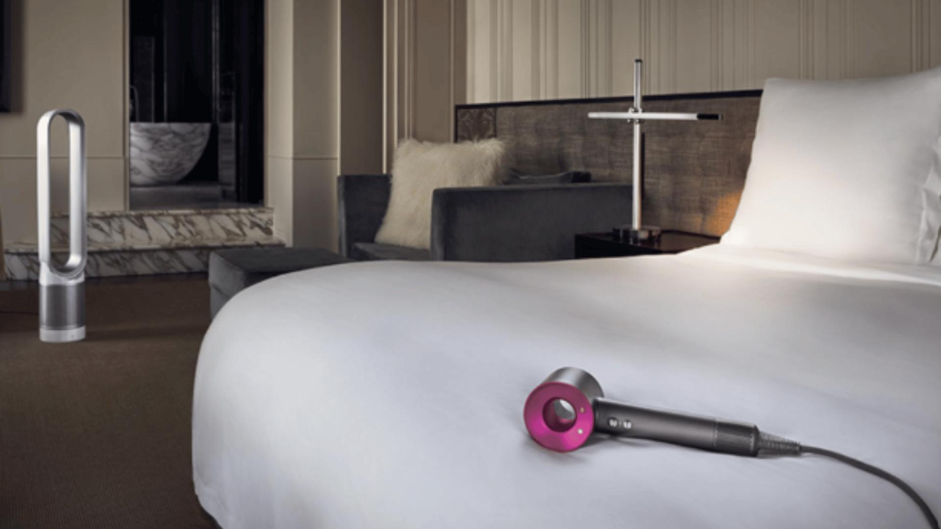 Dyson hair dryer placed on a hotel bed in a modern room.