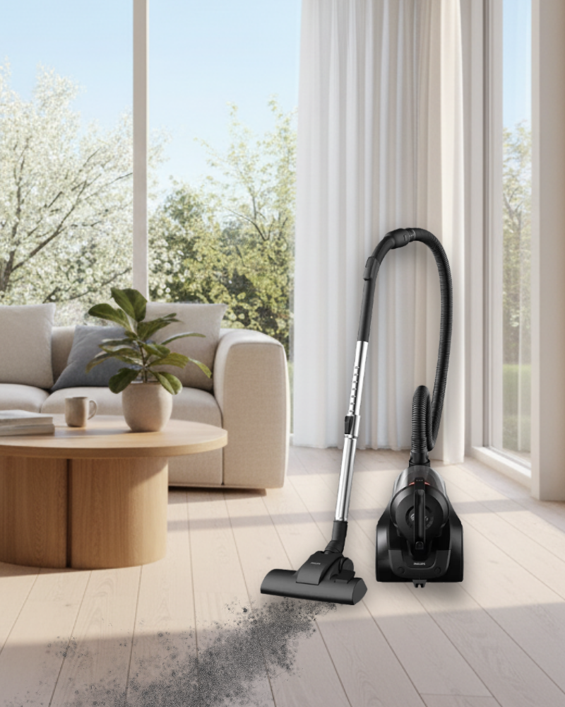 Philips bagless vacuum cleaner on light wood flooring, sucking up spilled dust beside a bright sofa, coffee table, and window view.