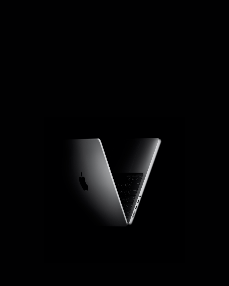 Apple MacBook Pro with M5 chip, half-open, in dramatic lighting, showing its slim aluminium body and keyboard on a black background.
