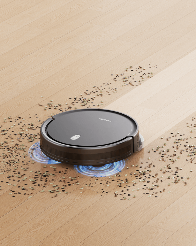 Xiaomi robot vacuum gliding across pale wood floor, scrubbing scattered crumbs with twin rotating mop pads.