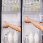 A person sliding the refrigerator’s door pocket up and down to change its height, with various bottles stored on the shelves.
