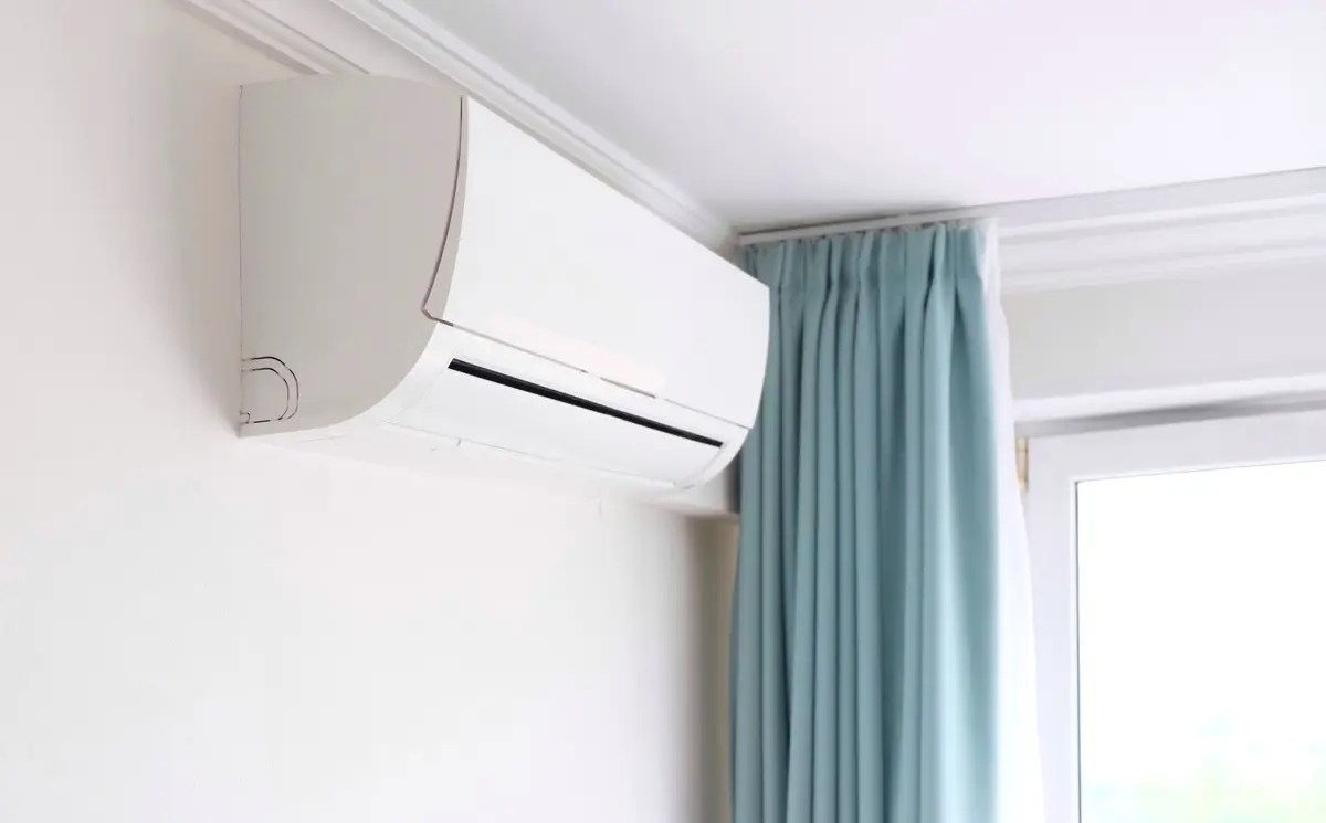 Modern white air conditioner mounted on a wall near blue curtains. Discover the best inverter aircond in Malaysia.