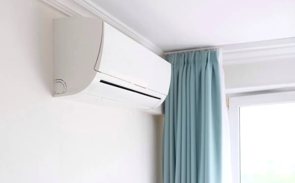 Modern white air conditioner mounted on a wall near blue curtains. Discover the best inverter aircond in Malaysia.